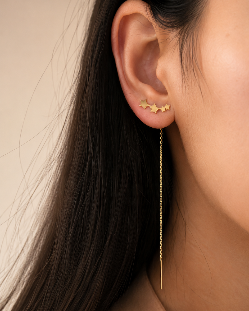 Close-up of a person wearing a gold star earring with a dangling chain.