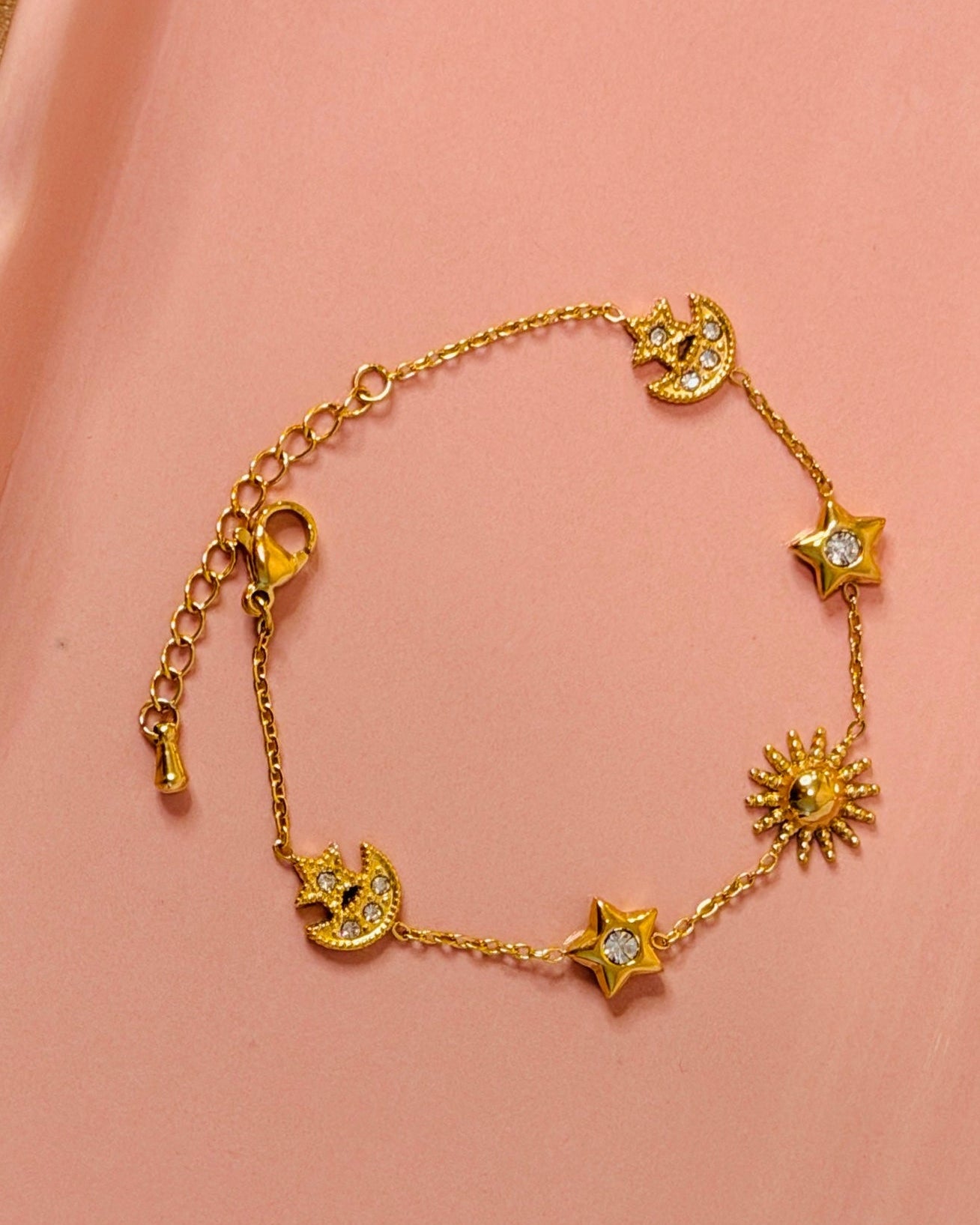 Gold bracelet with star and moon charms on a pink surface